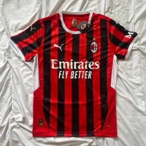 AC Milan hemmatröja Puma - Säljer en klassisk AC Milan fotbollströja från Puma med röda och svarta vertikala ränder, vita detaljer och klubbmärke på bröstet. Tröjan har sponsortryck från Emirates och MSC samt vit krage och ärmslut.