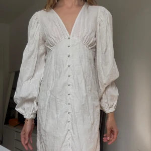 Vit broderad klänning med puffärmar - Superfin vit klänning med broderade blommor, puffiga långärmar och v-ringning. Klänningen har knappar framtill och lätt markerad midja. Perfekt för skolavslutning, student eller bara för sommarens tillfällen!🌸💕