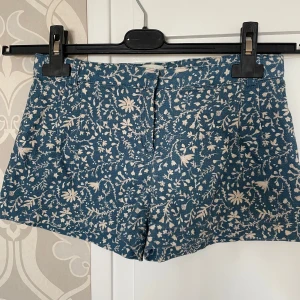 Blå blommiga shorts från Mango - Säljer ett par blå shorts från Mango med vitt blommigt mönster. Shortsen har ett grövre tyg än vad ” vanliga ” shorts har men även om så är det ett par super fina sommar shorts ☀️Shortsen är i storlek 11 till 12 år men jag som är 14 använde dem förra sommaren när jag var 13. 