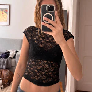 Svart spets topp med kort ärm - Säljer en svart, tight och croppad topp i spets med korta ärmar. Toppen har ett transparent blommigt spetsmönster och kan användas på två sätt. Antingen med öppen rygg eller med en fin urringning fram. Perfekt att styla med jeans eller kjol för en trendig look. Superfin att ha på fest!✨