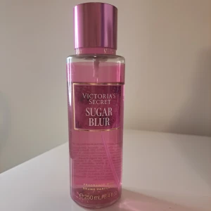 Victoria's Secret Sugar Blur Body Mist - En söt och fräsch body mist från Victoria's Secret med doft av vispad vaniljsocker, bärnsten och hallon. Flaskan är genomskinlig med rosa toner och har ett glansigt rosa lock. Rymmer 250 ml.