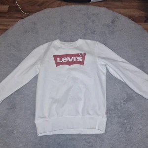 Vit sweatshirt från Levi's - Säljer en vit sweatshirt från Levi's med klassisk röd logga framtill. Tröjan har rund halsringning och långa ärmar. Perfekt för en avslappnad och stilren look.