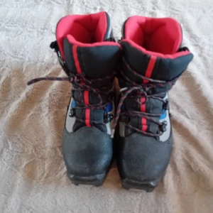Salomon pjäxor med snörning - Säljer ett par Salomon pjäxor i svart, grått och blått med röda detaljer. Kängorna har snörning och hög modell som ger bra stöd och värme. Perfekta för kalla dagar och vinteraktiviteter.