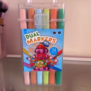 Dual Markers 24-pack - Säljer ett set med 24 färgglada dual markers i plastetui. Pennorna har två spetsar, en tunn och en bred, och finns i många olika nyanser som rosa, blå, grön, orange och gul. Perfekt för teckning, färgläggning och kreativt skapande.