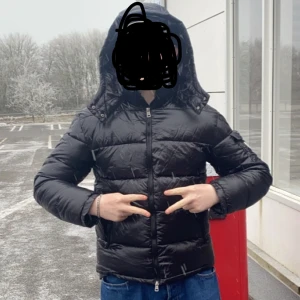 Moncler jacka - Säljer en svart Moncler dunjacka med huva och dragkedja. Jackan har klassisk pufferstil och Moncler-logga på ärmen. Perfekt för kyliga dagar och riktigt snygg till jeans eller sweatpants. Taggen går att skanna så kommer man in på moncler hemsidan :)