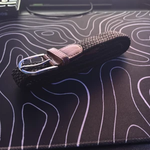 Flätat svart bälte med bruna skinn-detaljer - Säljer ett stilrent svart flätat bälte med snygga bruna skinn-detaljer vid spännet. Bältet har ett klassiskt silverfärgat spänne och passar perfekt till jeans eller chinos. Enkel och tidlös design som lyfter din outfit.