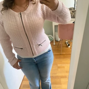 Ljusrosa stickad kofta  - Säljer en ljusrosa stickad kofta från Isolde med dragkedja framtill och två dekorativa fickor med dragkedja. Koftan har lång ärm och är i ett luftigt, virkat mönster. Perfekt att slänga på sig över en topp.