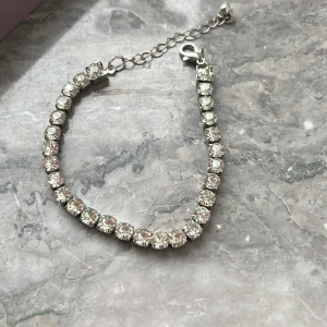 Glittrigt armband med stora stenar - Säljer ett snyggt armband med stora, glittrande stenar i silverfärg. Armbandet har justerbar kedja och passar perfekt för att ge extra bling till din outfit. Enkel att ta på med karbinhake.