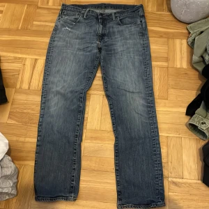 Levi's blå jeans straight fit - Klassiska blå jeans från Levi's med rak passform och femficksdesign. Jeansen har normal midja och subtil slitning vid fickan fram. Perfekta för en avslappnad stil och passar till det mesta. Storlek 36/30.