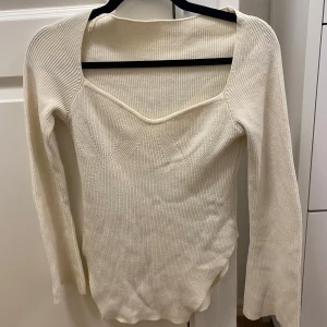 Krämvit ribbad stickad tröja med unik halsringning - Säljer en krämvit stickad tröja med lång ärm och snygg, djup fyrkantig halsringning. Tröjan är ribbad och har en figurnära passform som framhäver siluetten. Perfekt för dig som gillar stilrena och trendiga plagg.