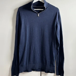 Marinblå tröja med dragkedja från Jack & Jones - Snygg marinblå tröja från Jack & Jones med halv dragkedja i halsen. Tröjan har lång ärm och ribbade muddar vid ärmslut och nederkant. Perfekt för lager-på-lager och enkel att matcha med jeans eller chinos.