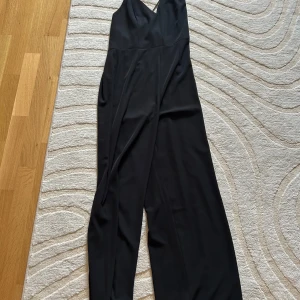 Svart jumpsuit med smala axelband från Bik Bok - Säljer en svart lång jumpsuit från Bik Bok med smala axelband och v-ringad hals. Jumpsuiten har en elegant och stilren design med raka ben och dragkedja i sidan. Storlek S men passar nog mer S/M,M. Väldigt stretchigt & mjukt material. Aldrig använd. Säljer då den var för stor för mig. 