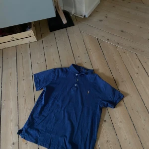 Ralph Lauren piké  - Ralph Lauren pikétröja i en något ljusare blå nyans. Märkt storlek L i barnstorlek, men passar som en vuxen S – smal passform (slim fit). Använd, i okej skick. Inga hål eller fläckar. Stilren och klassisk – perfekt för dig som gillar en tajtare passform och ikonisk design.