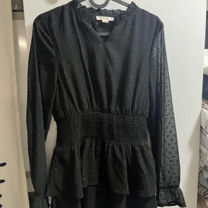 Svart prickig klänning från Gina Tricot - Supersöt svart klänning från Gina Tricot med små diskreta prickar och volangdetaljer. Klänningen har lång ärm med resår vid ärmslut, markerad midja och lätt volang nertill. Perfekt för dig som gillar en feminin och trendig stil. Helt oanvänd. Så fin klänning till, exempel skolavslutning! 🌸☀️