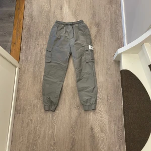 Grå cargobyxor från Jordan - Säljer ett par grå cargobyxor från Jordan med resår i midjan och bensluten. Byxorna har flera fickor på sidorna och en klassisk cargomodell. Perfekta för en avslappnad streetstil.