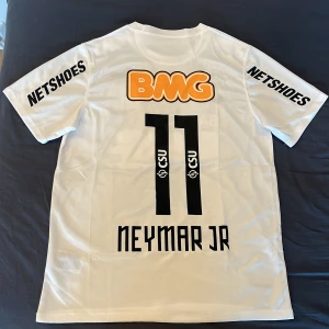 Vit Santos Neymar Jr fotbollströja - Santos FC matchtröja i vitt med svarta detaljer, Neymar Jr och nummer 11 på ryggen. Broderat klubbmärke med två stjärnor, sponsorloggor och Nike Swoosh på bröstet. Tillverkad i lätt och ventilerande material.