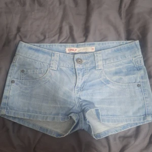Ljusblå jeansshorts från ONLY - Säljer ett par ljusblå jeansshorts från ONLY med klassisk femficksdesign och knappgylf. Shortsen har bälteshällor och är i en kort modell som passar perfekt till varma dagar. Vintage.