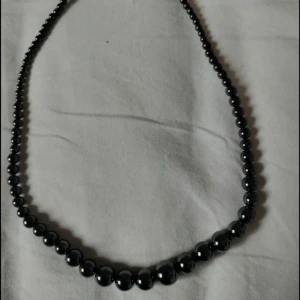 Svart pärlhalsband - Elegant halsband med svarta pärlor i olika storlekar. Klassisk design som passar perfekt till att lyfta en outfit. Halsbandet har ett enkelt spänne och pärlorna har en fin glans.