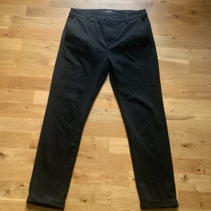Svarta chinos från Oscar Jacobson - Snygga svarta chinos från Oscar Jacobson med klassisk passform. Byxorna har normal midja, raka ben och diskreta fickor både fram och bak. Perfekta för en stilren look.