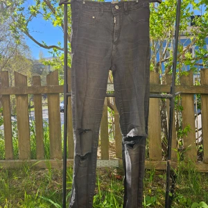 Svarta skinny jeans med slitningar hög midja - Säljer ett par svarta skinny jeans med slitningar på båda knäna. Jeansen har klassisk femficksdesign, dragkedja och knapp framtill. Perfekta för en avslappnad och trendig look. Strl 29/32