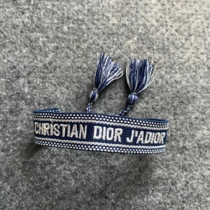 Christian Dior J'Adior armband med tofsar - Säljer 3 snyggt armband från Christian Dior med texten 'J'ADIOR'. Armbandet har tofsar i ändarna och finns i tre olika färger: blå, svart och beige. Perfekt accessoar för att lyfta din outfit.