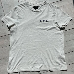 Vit t-shirt från A.P.C. - Säljer en klassisk vit t-shirt från A.P.C. med diskret logga tryckt på bröstet. T-shirten har rund halsringning och korta ärmar. Perfekt basplagg med stilren design och skön passform.