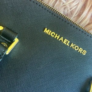 Svart handväska från Michael Kors - Säljer en stilren svart handväska från Michael Kors med guldfärgade detaljer. Perfekt accessoar för att lyfta din outfit!❣️