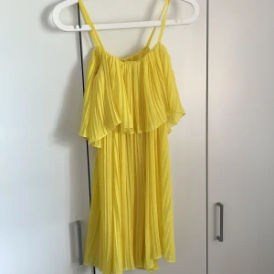Gul plisserad sommarklänning med volang - Säljer en solgul plisserad klänning med smala axelband och volang. Klänningen är luftig och har en flowy känsla, perfekt för varma dagar💛