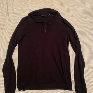 Svart långärmad pikétröja - En stilren svart långärmad pikétröja med krage och knappar framtill. Perfekt för en enkel och klassisk look. Tröjan har en normal passform och är tillverkad i ett mjukt material.