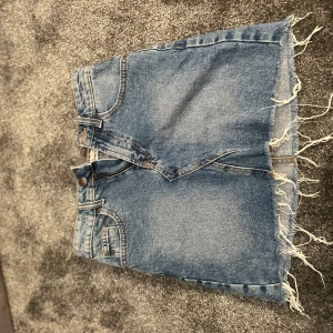 Blå jeanskjol med fransad kant från Denim Co - Säljer en blå jeanskjol från Denim Co med fransad nederkant och klassiska fickor både fram och bak. Dock är dragkedjan sönder men går lätt att lösa 
