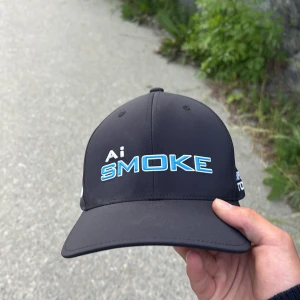 Svart keps från Callaway Ai Smoke - Svart keps med böjd skärm från Callaway. Framtill står det 'Ai SMOKE' i vitt och blått, på sidan 'CHROME TOUR' och 'Callaway' samt 'Odyssey' broderat baktill. Justerbar passform med kardborreband.