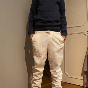 Vita linnebyxor från Jack & Jones - Säljer ett par vita linnebyxor från Jack & Jones med avslappnad passform och resår i midjan. Byxorna har fickor både fram och bak och är perfekta för en chill och stilren look. Storlek 164 men passar folk upp mot 170 modell är 169 lång