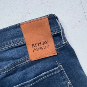 Replay Hyperflex jeans med slitningar - Säljer ett par blå Replay Hyperflex jeans med snygga slitningar och lätt tvättad look. Jeansen har klassisk femficksdesign och slim passform med måtten 32/32. Dock kortade till mig som är ca 180.