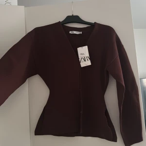 Mörkbrun kavaj från ZARA - Säljer en stilren mörkbrun tröja (eller vad man ska kalla de) från ZARA i storlek XS.  v-ringad halsringning och knäppning framtill. Passformen är figurnära och modellen är klassisk, perfekt för en snygg och enkel look.