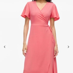 Blommig omlottklänning från VILA - Säljer en söt blommig omlottklänning från VILA i rosa och röda toner. Klänningen har korta ärmar, v-ringning och knyt i midjan. Perfekt för sommarens alla tillfällen!