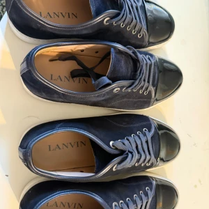  Lanvins - Säljer ett par stilrena blå sneakers från Lanvin med svart, glansig tå och vita sulor. Skorna har snörning och silverfärgade öljetter. Perfekta för dig som vill ha en klassisk men ändå unik look. Har två lika par. Båda har kvitto och allt ingår och jag säljer båda för 5000, men pris går att diskutera