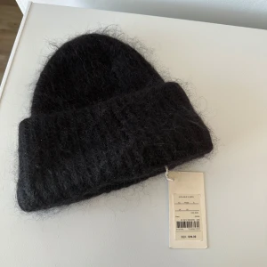 Svart fluffig mössa - Mysig svart mössa med fluffig yta och bred uppvikt kant. Perfekt för kyliga dagar och ger en trendig look. Mössan är enkel att matcha med olika outfits och har en klassisk form.
