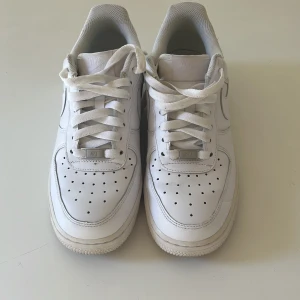 Vita Nike Air Force 1 sneakers - Klassiska vita Nike Air Force 1 sneakers med snörning och perforerad tå för extra ventilation. Skorna har en platt sula och är tillverkade i skinn med diskreta detaljer. Perfekta för en stilren och tidlös look. Scick 8/10 då det finns tecken på användning men inte nånting som stör priset är diskuterbart och tveka inte på att hör av er vid funderingar