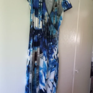 Blåmönstrad klänning med v-ringning - Säljer en klänning med abstrakt blått och vitt mönster. Klänningen har v-ringad hals och korta ärmar. Materialet känns mjukt och stretchigt, perfekt för varma dagar. Snygg passform som faller fint längs kroppen.