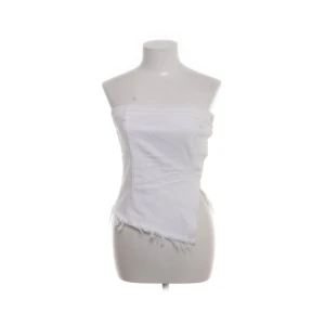 Vit zara tubtopp med fransad kant - Säljer en vit tubtopp från ZARA med fransad nederkant och smockad rygg för extra komfort. Toppen har en asymmetrisk skärning framtill och är perfekt för varma dagar.🩷🩷