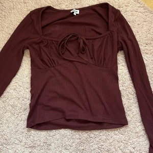 Vinröd ribbad topp med knyt  - Vinröd långärmad topp från Bubbleroom i ribbat material. Toppen har en söt knytdetalj framtill och en smickrande, figurnära passform. Perfekt att styla med jeans eller kjol för en trendig look.