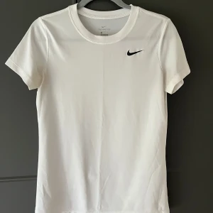 Vit tränings t-shirt från Nike - Säljer en vit t-shirt från Nike med Nike märket på bröstet. Använd väldigt lite, dock har Nike märket lite slitage (syns ej tydligt). Annars i mycket bra skick!💕