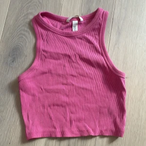 Rosa ribbad linnetopp - Säljer en rosa ribbad linnetopp i croppad modell. Toppen har ärmlös design och rund halsringning, perfekt för varma dagar eller som lager under en skjorta. Enkel och stilren med stretchigt material. passar även S
