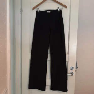 Svarta kostymbyxor med vida ben - Snygga svarta kostymbyxor med normal midja och vida ben. Klassisk modell som passar till många olika stilar. Byxorna har en stilren look utan synliga detaljer framtill. 