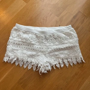 Vita spets-shorts med fransar - Superfina vita shorts med spets och dekorativa fransar längst ner. De har elastisk midja och ett detaljerat spetsmönster över hela shortsen. Perfekta för varma dagar och ger en bohemisk känsla.
