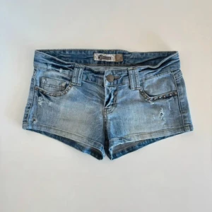 Blå jeanshorts - Så snygga blå lågmidjade jeansshorts med slitna detaljer och små nitar längs fickorna. Måtten står på bild två, kom privat för fler bilder och frågor💕