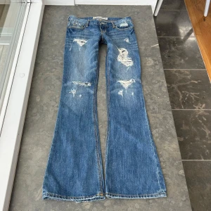 Hollister bootcut håliga jeans  - Säljer nu mina snyggaste hollister bootcut, lowwaist jeans! Sjukt coola detalijer och hål och perfekta nu till sommaren. Midjemått: ca 38-39 cm. Midjehöjd: ca 17 cm innerbenslängd: ca 83 cm💕 Skulle uppskatta att de är ca storlek S💕