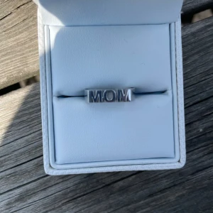 Silverring med texten MOM från Edblad  - Säljer en stilren silverring med texten MOM framtill, från Edblad. Ringen har en fyrkantig form och är tillverkad i blankt silverfärgat material. Perfekt som present till någon speciell.