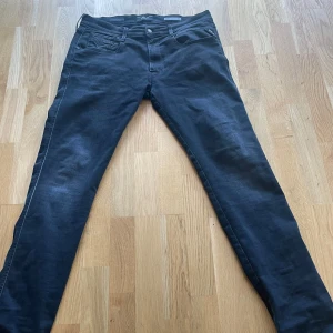 Svarta Replay Anbass jeans - Säljer ett par svarta Replay Anbass jeans med klassisk femficksdesign och raka ben. Jeansen har diskreta detaljer och en snygg tvätt. Storlek 34/34, knappt använda