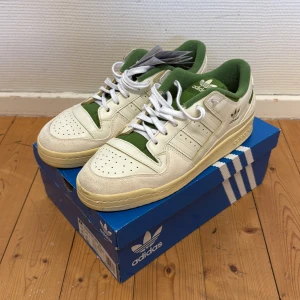 Adidas Forum sneakers med gröna detaljer - Säljer ett par Adidas sneakers i vitt med gröna detaljer och vit sula. Skorna har klassisk snörning, perforerad tå och grönt innerfoder. Perfekta för dig som gillar retrostil och vill sticka ut med en unik färgkombo. 46 men sitter som 45 - 45,5 